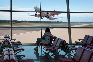 Young woman waiting for flight time at the airport, in the background a plane is being prepared for flight - istanbul