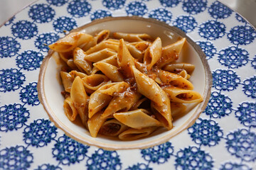 Close-up of penne pasta bolognese served in a white and blue ceramic bowl with rich, meaty sauce. This image is perfect for illustrating delicious Italian cuisine, comfort food, or food presentation.