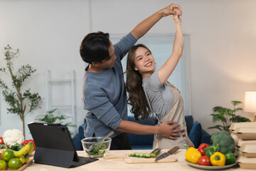 Young asian couple enjoying a lively dance while preparing fresh organic vegetables and fruits for a nutritious meal in their modern kitchen, radiating love and happiness
