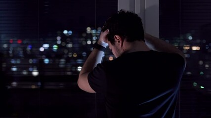 Depressed man standing by the window at night