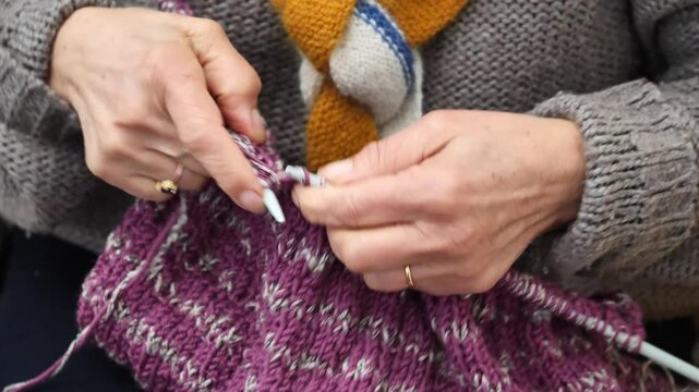 Person is knitting a purple sweater with a striped pattern. The person is using a knitting needle to work on the sweater