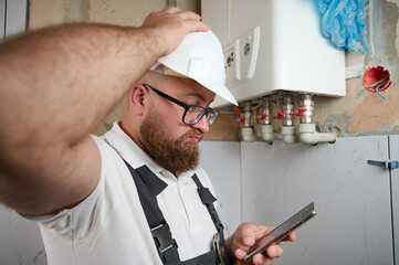 Plumber Install Boiler.Professional engineer installing gas boiler at home and checking the connections and pipes of the domestic heating system using smartphone.Boiler Installation Service adjusting.