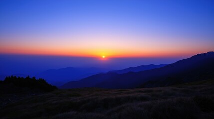Fototapeta premium Dawn breaking over mountains with blue sky distant silhouette of orange sun rising in horizon light navy blues at dawn deep purples