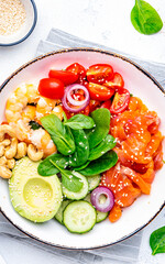 Salad bowl with salmon, shrimps, avocado, spinach, vegetables, sesame and cashew nuts for keto diet. White background, top view