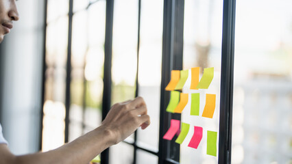 Man organizing project tasks Colorful sticky notes on glass of meeting room