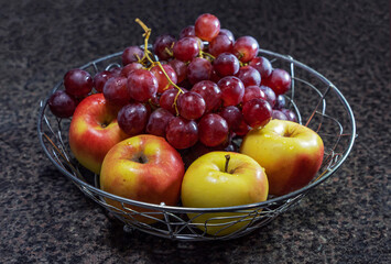In a metal fruit bowl there are four freshly washed apples and two branches of large red grapes, fruits of late ripening varieties.