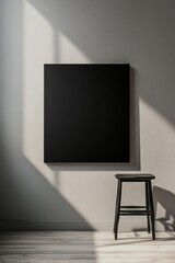 A minimalist room featuring a black canvas and wooden stool, bathed in natural sunlight casting soft shadows on neutral walls.