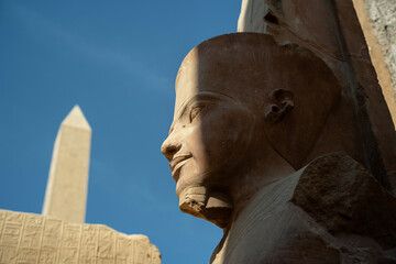 Statue of a pharaoh with an abelisk in the background in Luxor