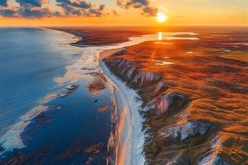 Naklejka premium A breathtaking aerial view of the sun setting over Sylt's coastline, creating an enchanting atmosphere with warm hues across land and sea, focusing on the stunning natural landscape.
