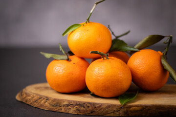 A pile of whole mandarine fruits with leaves on wooden plate, grey table background