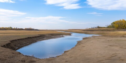A calm river meandering through open fields under a bright blue sky with scattered white clouds.
