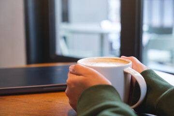 Hands holding a cup of coffee with laptop on the table