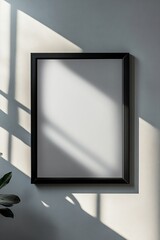 Fototapeta premium A black picture frame on a wall with sunlight casting shadows, creating a minimalist and tranquil setting.