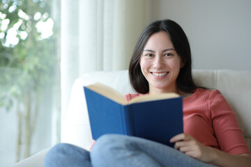 Happy asian woman holding paper book looking at you