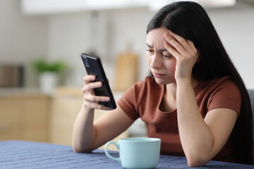 Worried asian woman checking smart phone in the kitchen