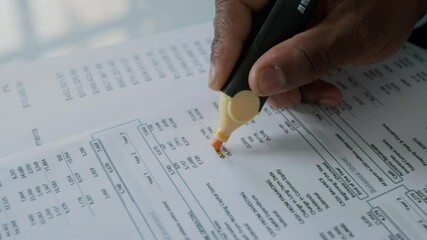 Close-up shot of hand of unrecognizable businessman using highlighter to mark key figures on financial document during analysis