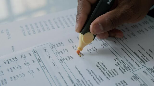 Close-up shot of hand of unrecognizable businessman using highlighter to mark key figures on financial document during analysis
