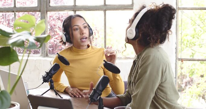 Two multiracial female colleagues recording podcast at home, engaging in lively conversation - Powered by Adobe