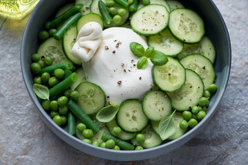 Bowl of salad with burrata cheese, fresh cucumber, green peas, beans and basil, horizontal shot, middle closeup