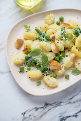 Potato gnocchi with different types of cheese, green peas, beans and basil, vertical shot on a white stone surface, middle close-up
