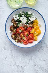 Plate with cherry tomato, green beans and blue cheese salad, above view on a white stone background, vertical shot with space