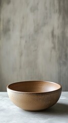A simple, rustic ceramic bowl placed on a concrete surface with a textured gray background, showcasing minimalist design.
