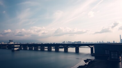 Obraz premium Serene cityscape view of a modern bridge spanning a tranquil river, showcasing a distant city skyline under a partly cloudy sky.