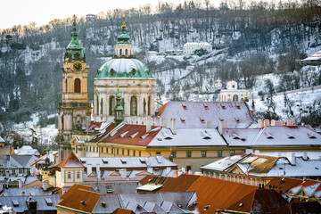 Scenic Winter View of Malá Strana in Prague with Snow-Covered Rooftops and St. Nicholas Church