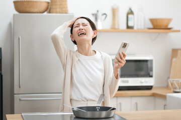 キッチンでスマホを持って悩む女性