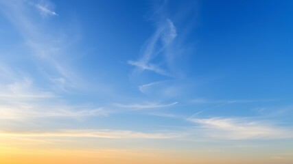 Obraz premium Serene sunset sky: a picturesque view of a vibrant, clear blue sky with wispy clouds at sunset, showcasing beautiful warm-toned hues.