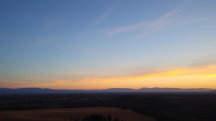 Obraz premium Serene sunset over rolling hills and distant mountains, a peaceful landscape panorama, captivating golden hour light,