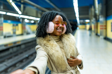 Young black woman smiling and taking selfie in subway station