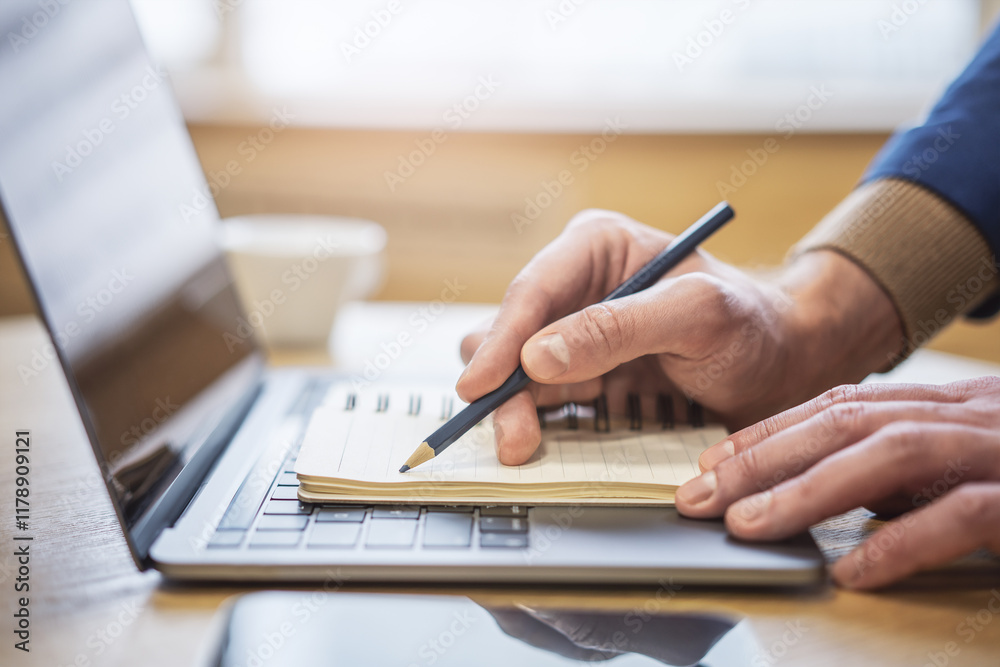 Poster Sharp view of a man's hand transcribing in a notepad on a cutting-edge laptop, with a defocused backdrop
