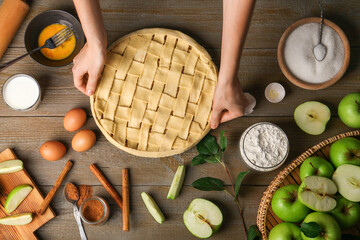 Woman making homemade apple pie and ingredients on wooden table, top view
