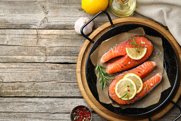 Fresh raw salmon steaks with spices in pan and products on wooden table, flat lay. Space for text