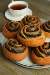 Tasty buns with poppy seeds and cup of tea on wooden table, closeup