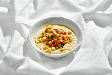 A fresh and healthy breakfast of oatmeal topped with a vibrant mix of diced tomatoes, avocado, and crunchy nuts.