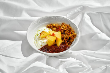 A bowl of homemade granola topped with fresh fruit, yogurt, and a drizzle of sweet jam.