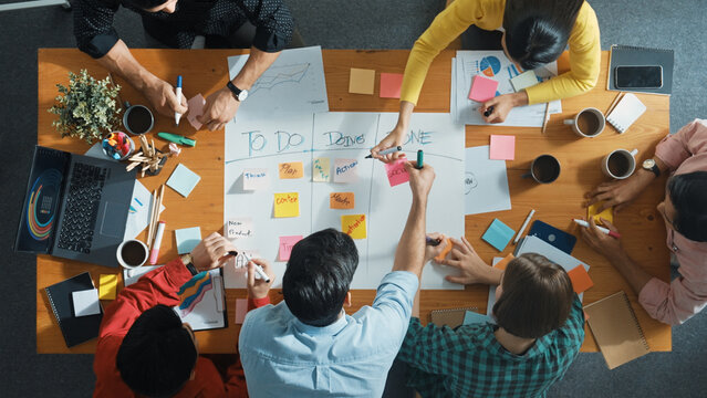 Top down aerial view of business team making scrum task board at meeting room. Group of people writing at paper and sticky notes for making kanban board to manage work flow. Top view. Convocation.