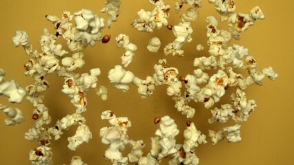 Slow motion shot of popcorn was throwing with yellow background. Fresh movie popcorn moving and falling. Popcorn in motion falling in a captivating dance. Dynamic movement and energy. Comestible.