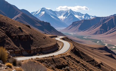 A scenic road winds through a dramatic desert landscape, with towering red rock cliffs and a clear blue sky in the background.