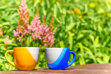 Tea time. Coffee break. Blue yellow cups on wooden in blooming garden