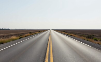 Fototapeta premium A scenic road winds through a dramatic desert landscape, with towering red rock cliffs and a clear blue sky in the background.