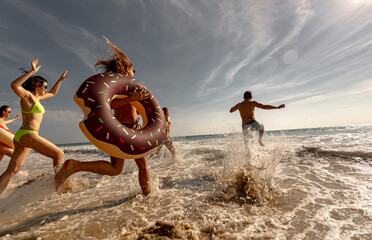 Big group of happy young friends are having fun, runs and jumps at sunset sea beach. Tropical vacations concept
