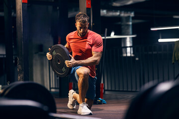 Portrait of fit strong sportsman doing lunges with weight plate at gym.