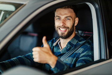 Portrait of smiling driver driving his car and giving thumbs up at the camera.