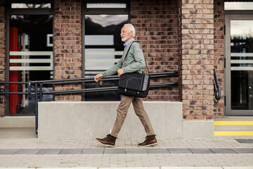 Side view of an old man in smart casual in rush walking on train station.