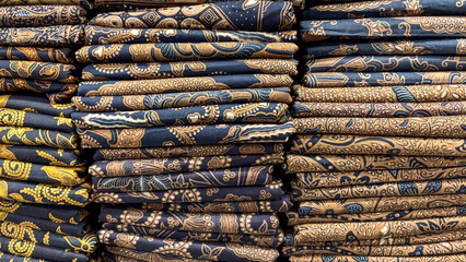Stacks of Exquisite Indonesian Batik Fabrics in Dark and Light Brown Hues Showcasing Intricate Traditional Patterns