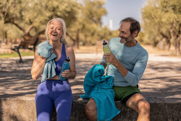 Senior couple resting and drinking water after exercising outdoors