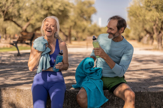Senior couple resting and drinking water after exercising outdoors - Powered by Adobe